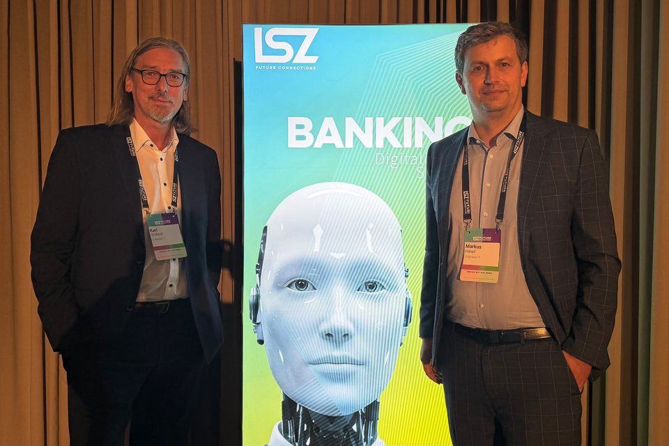 Geschäftsführer Karl Stöbich (links) und Geschaftsführer Markus Haspl (rechts) stehen vor einer großen Leinwand, auf der ein menschlich aussehender Roboter abgebildet ist.